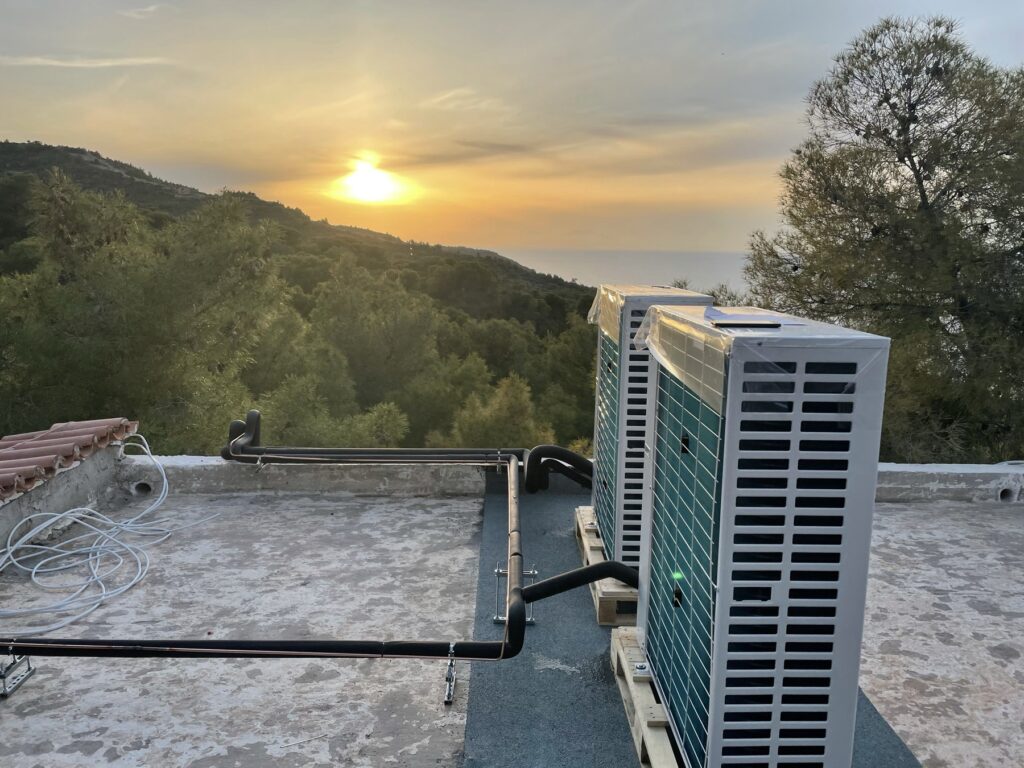 Εξωτερικές ψυκτικές μονάδες εγκατεστημένες σε ταράτσα με θέα σε δασική περιοχή και ηλιοβασίλεμα, τοποθετημένες από εξειδικευμένη ψυκτική εταιρεία.