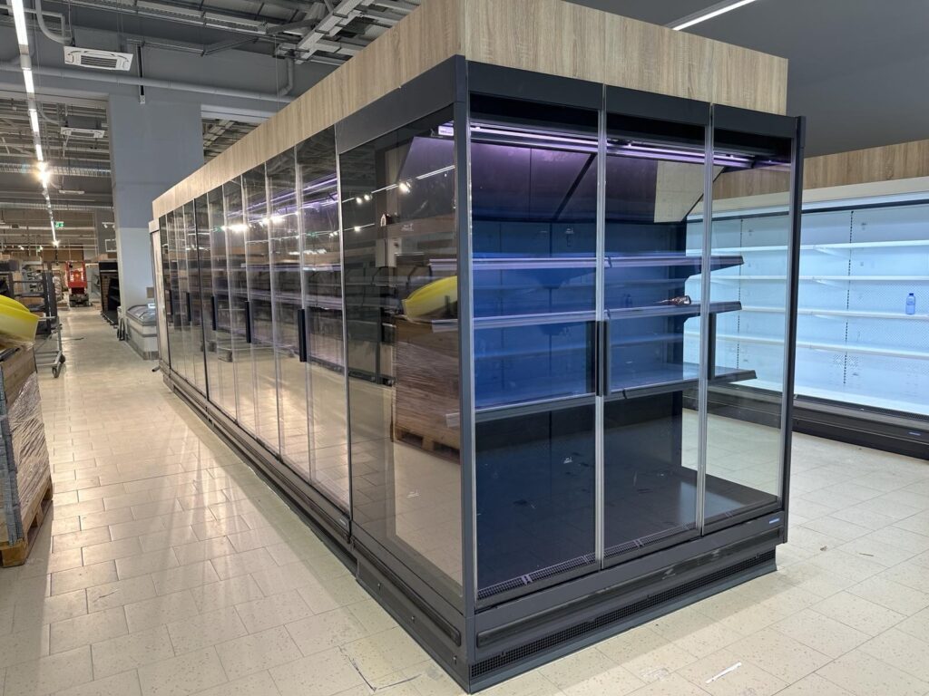 Μεγάλη εγκατάσταση επαγγελματικών ψυγείων βιτρίνας με LED φωτισμό σε σούπερ μάρκετ, ιδανικά για συντήρηση τροφίμων.